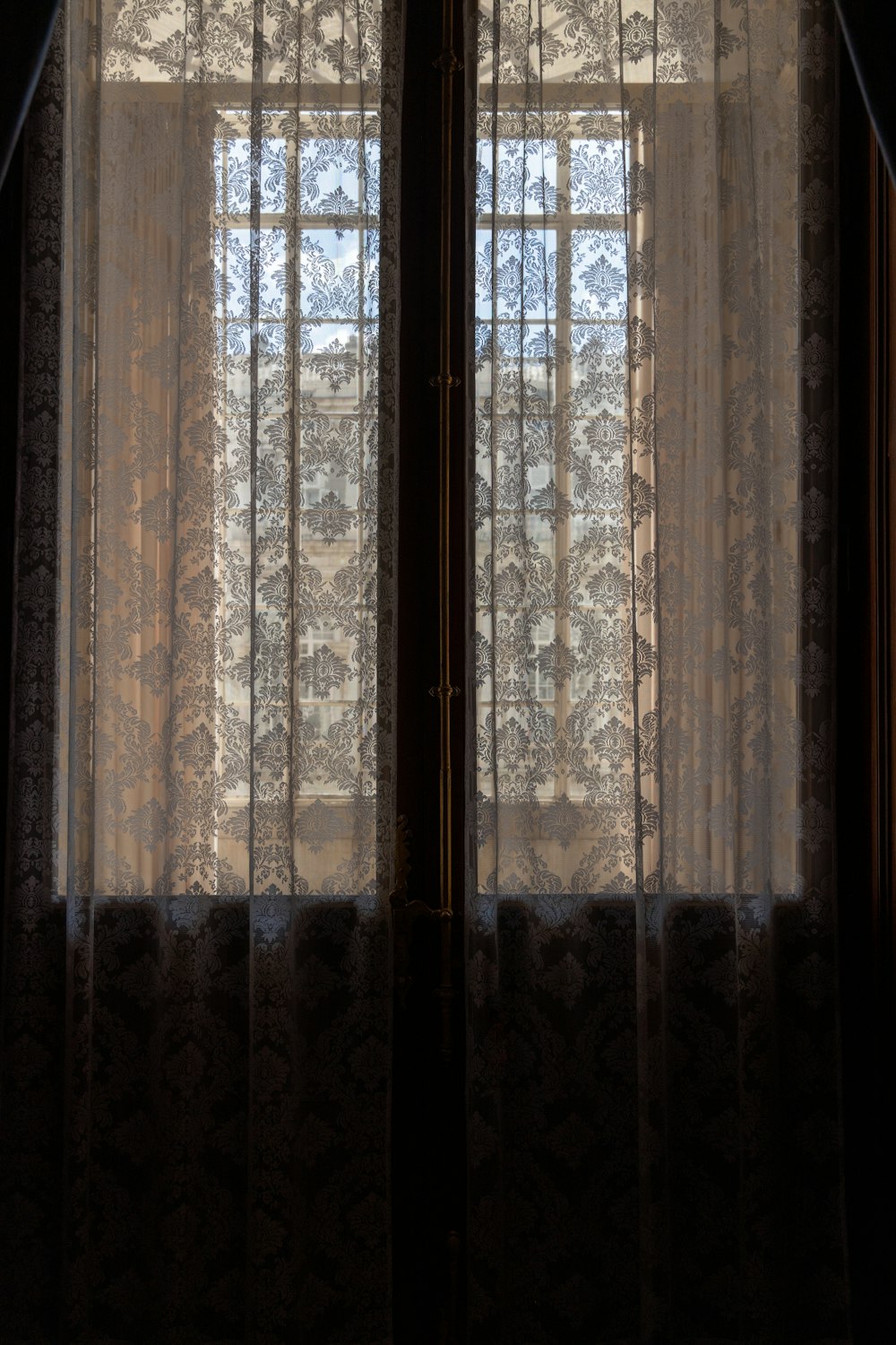 a window with sheer curtains and a cat sitting on the window sill