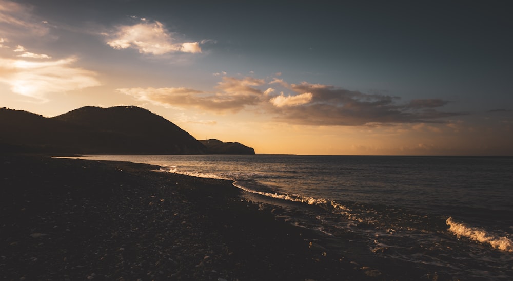 the sun is setting over the ocean with mountains in the background