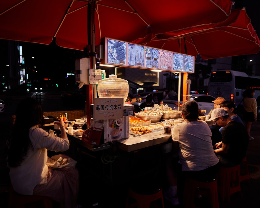 a group of people sitting at a table under a red umbrella