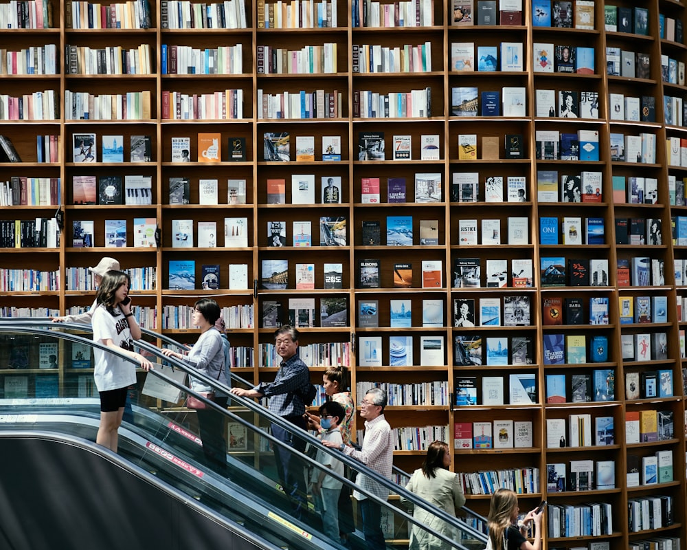 a group of people riding an escalator next to a wall of books