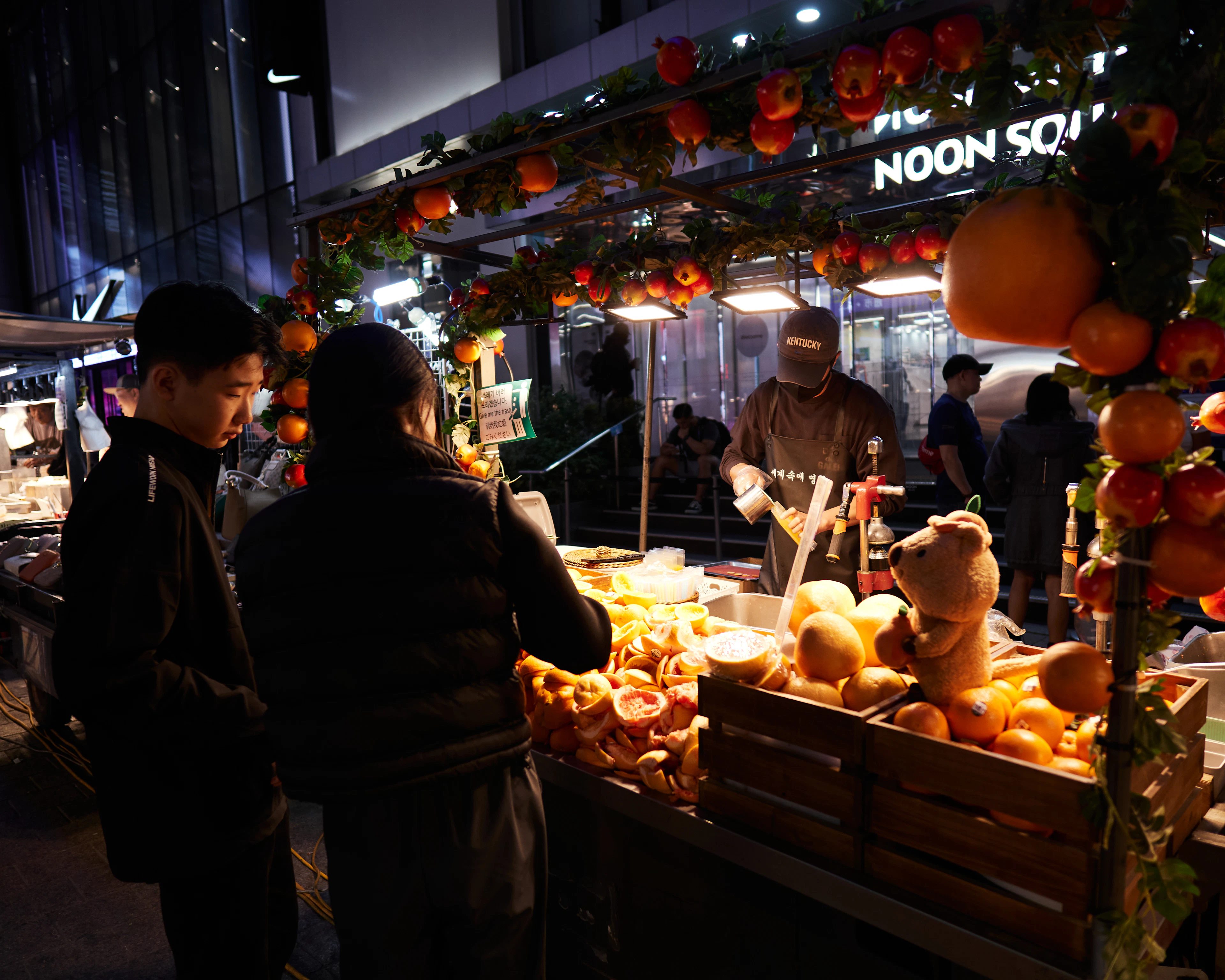 Shoppers browse a festively lit fruit stall piled with persimmons at a Seoul night market.