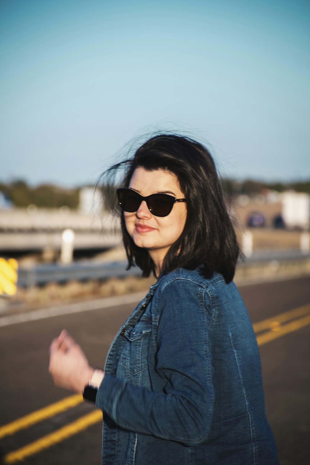 a woman wearing sunglasses standing on the side of a road