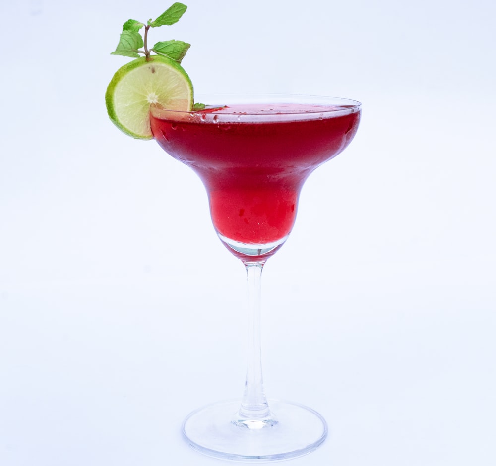 a red drink with a lime garnish on the rim
