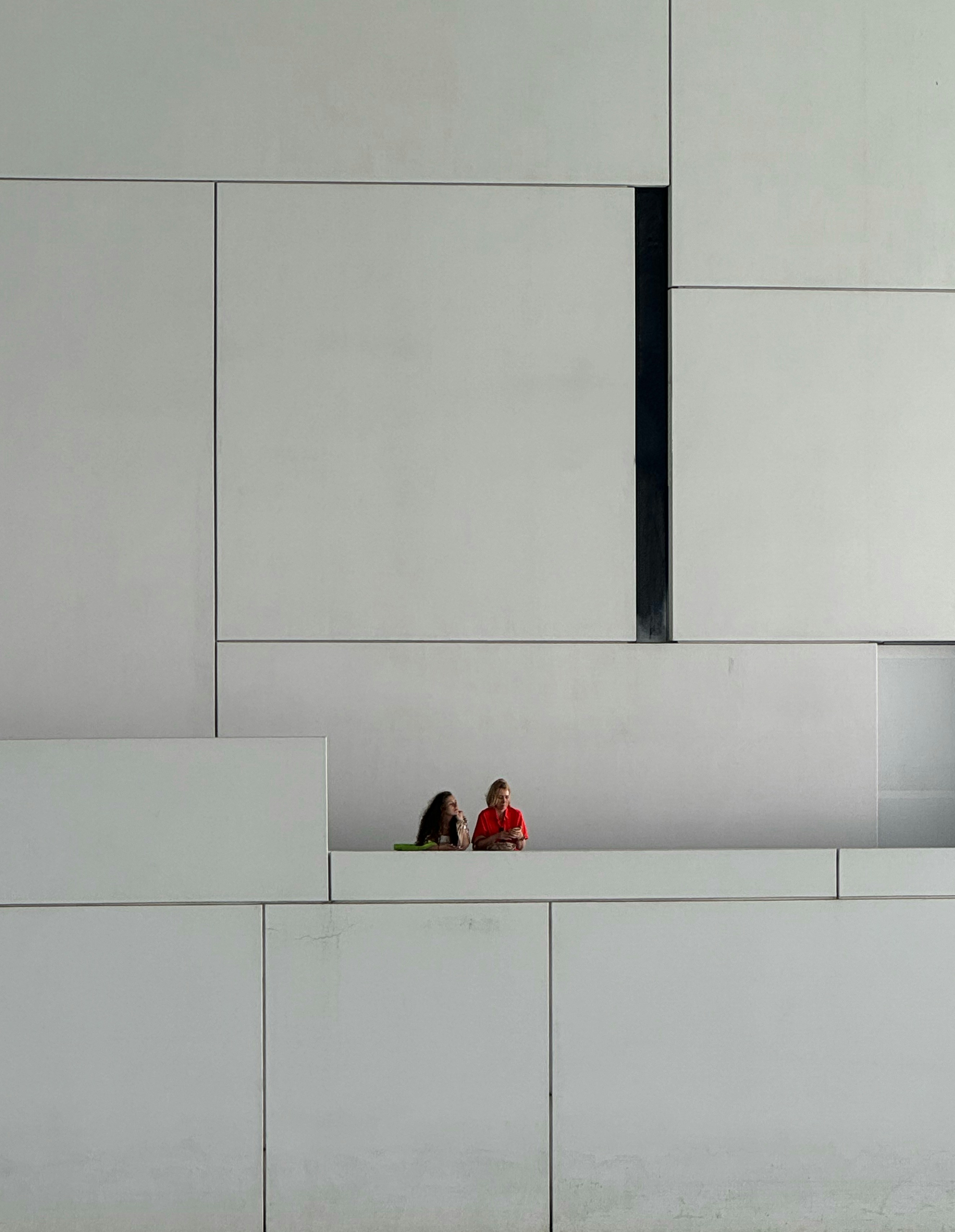two people sitting on a bench in front of a white wall