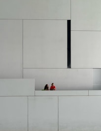 two people sitting on a bench in front of a white wall