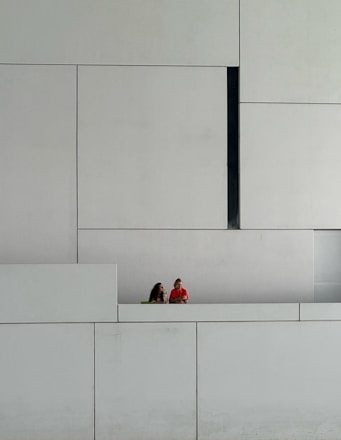 two people sitting on a bench in front of a white wall
