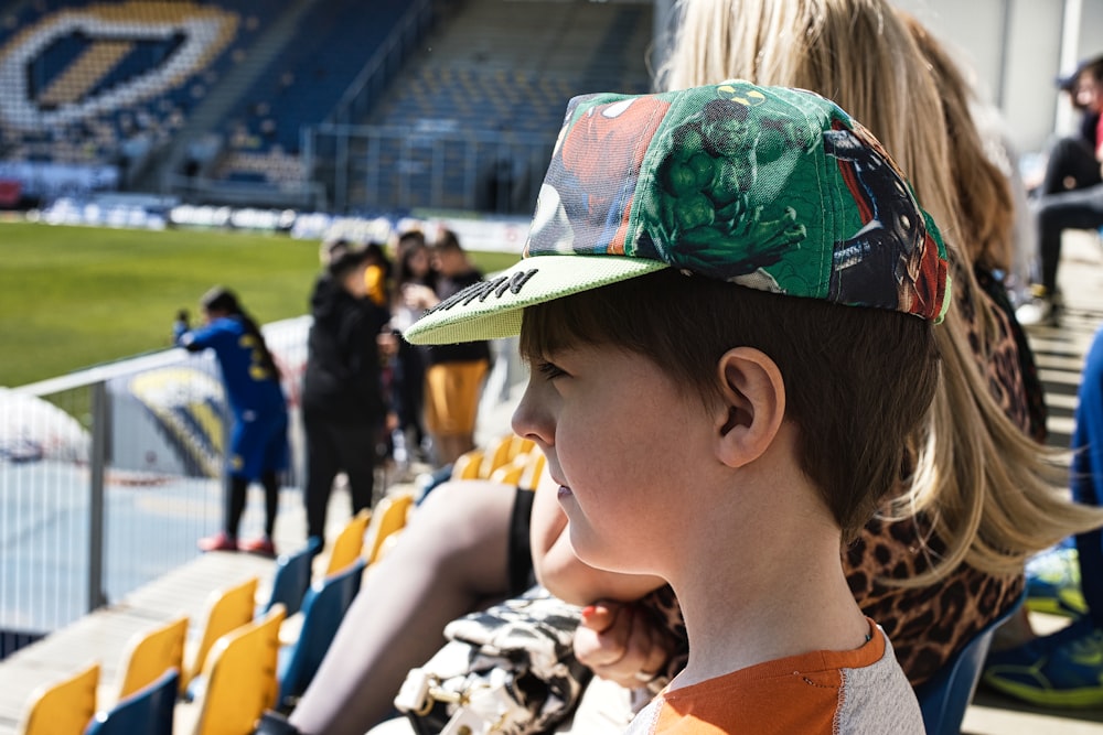 a young boy wearing a hat sitting in a stadium