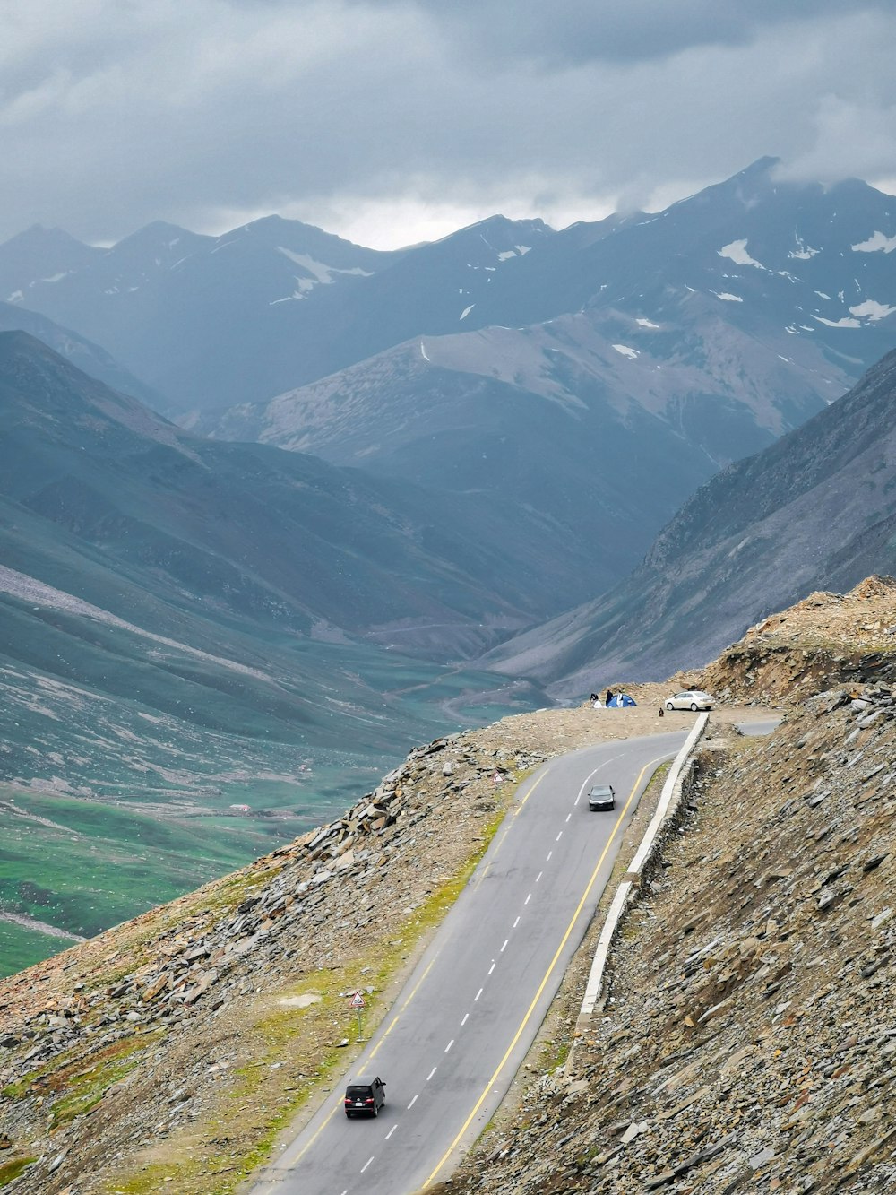 two cars driving down a mountain road with mountains in the background