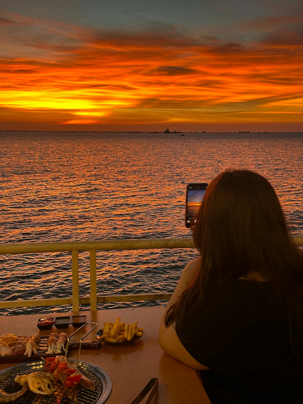 a woman taking a picture of a sunset over the ocean