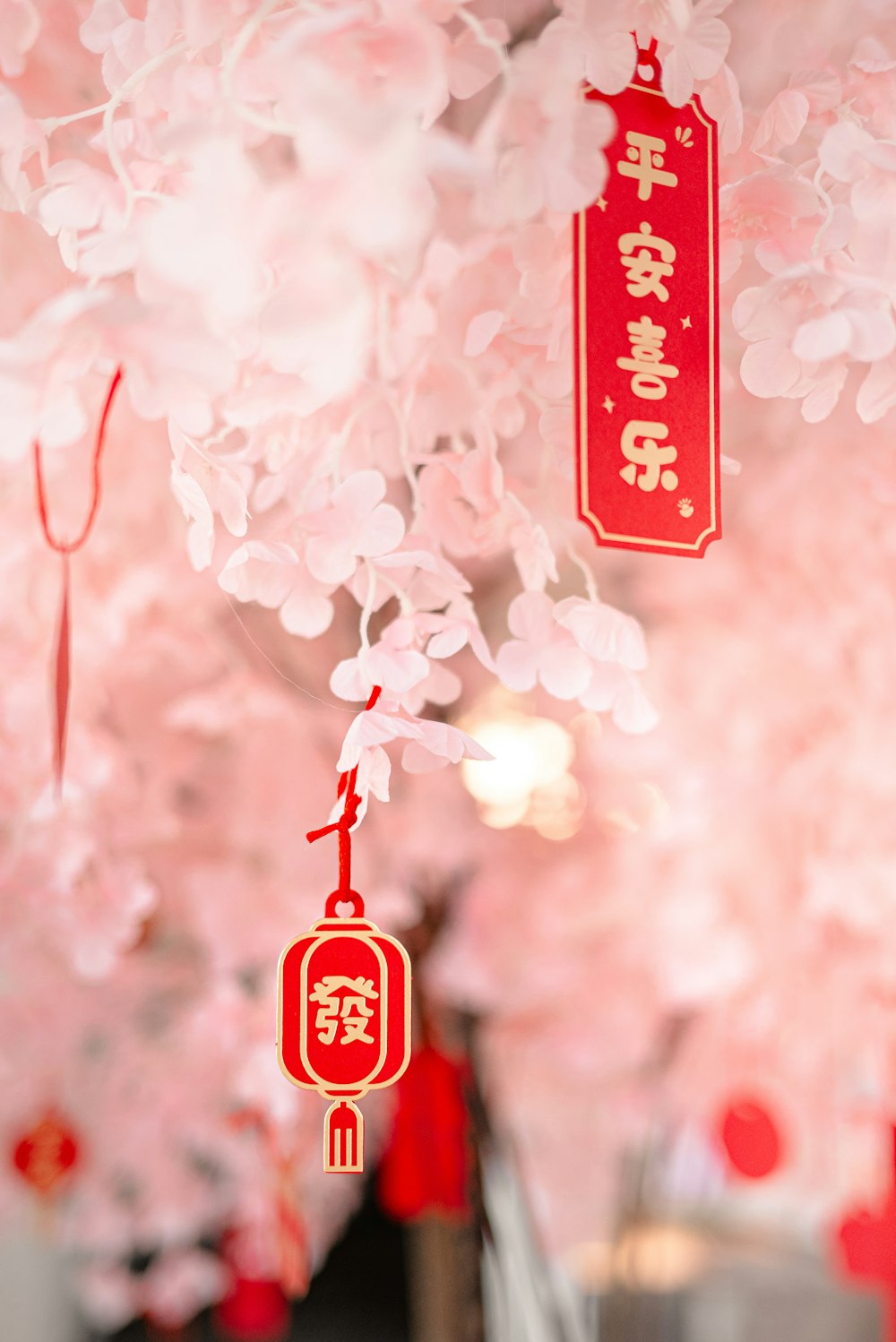 a red sign hanging from a tree filled with pink flowers
