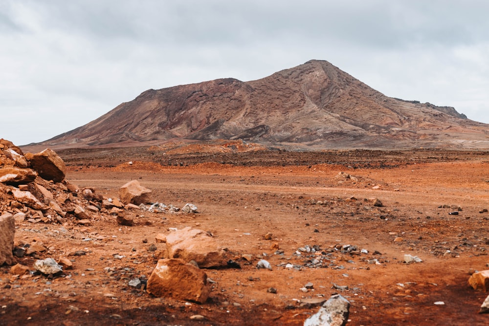 a dirt field with rocks and a mountain in the background