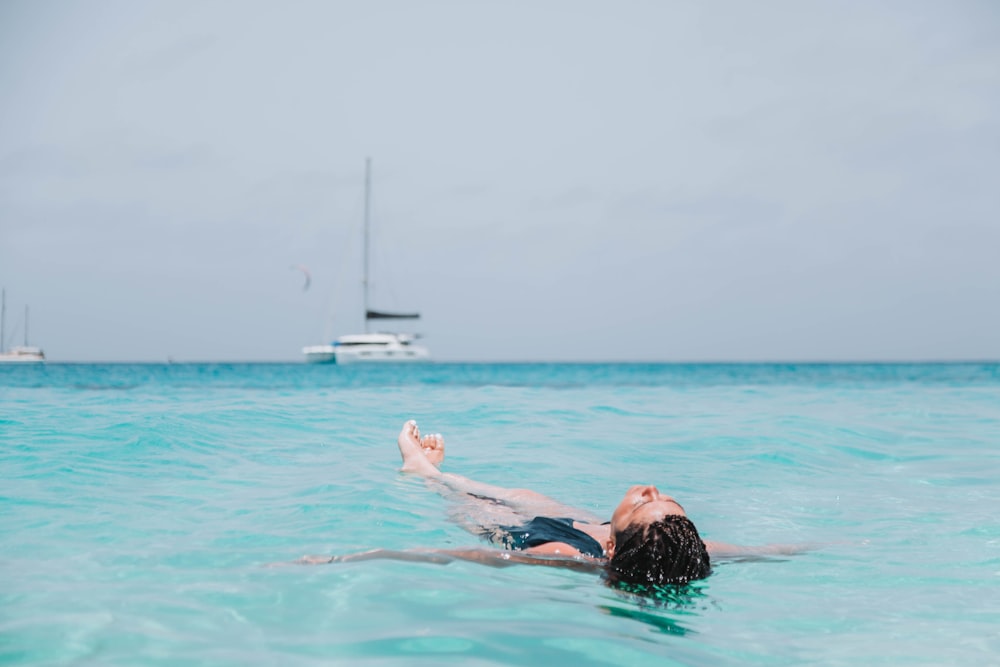 a woman swimming in the ocean with a sailboat in the background