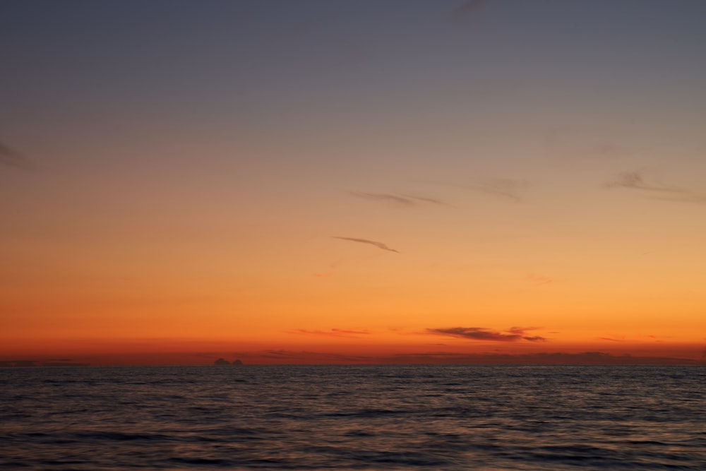 the sun is setting over the ocean with a sailboat in the distance