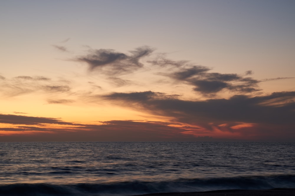 the sun is setting over the ocean on a cloudy day