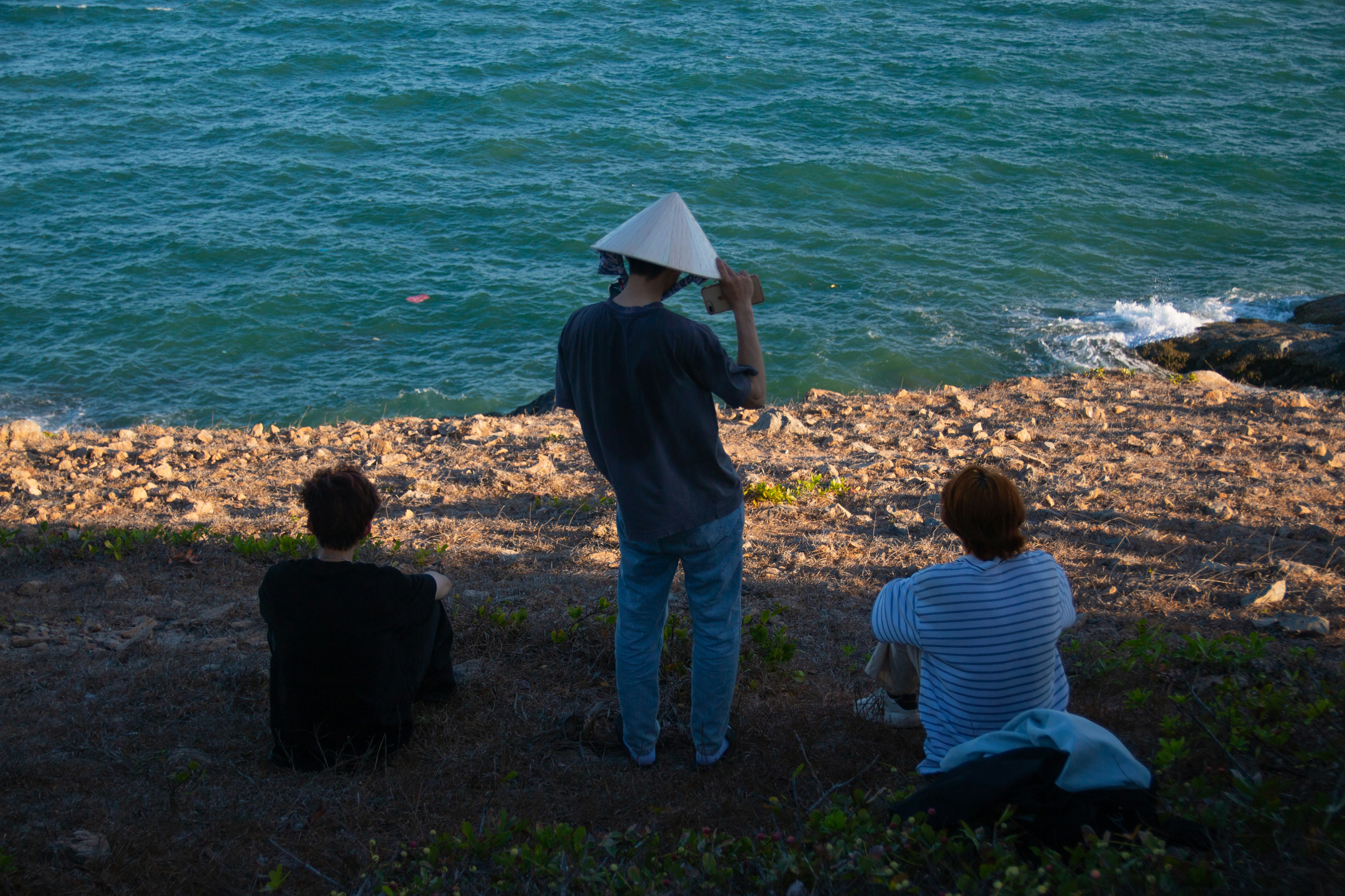 A group of people sitting next to a body of water photo – Free ...
