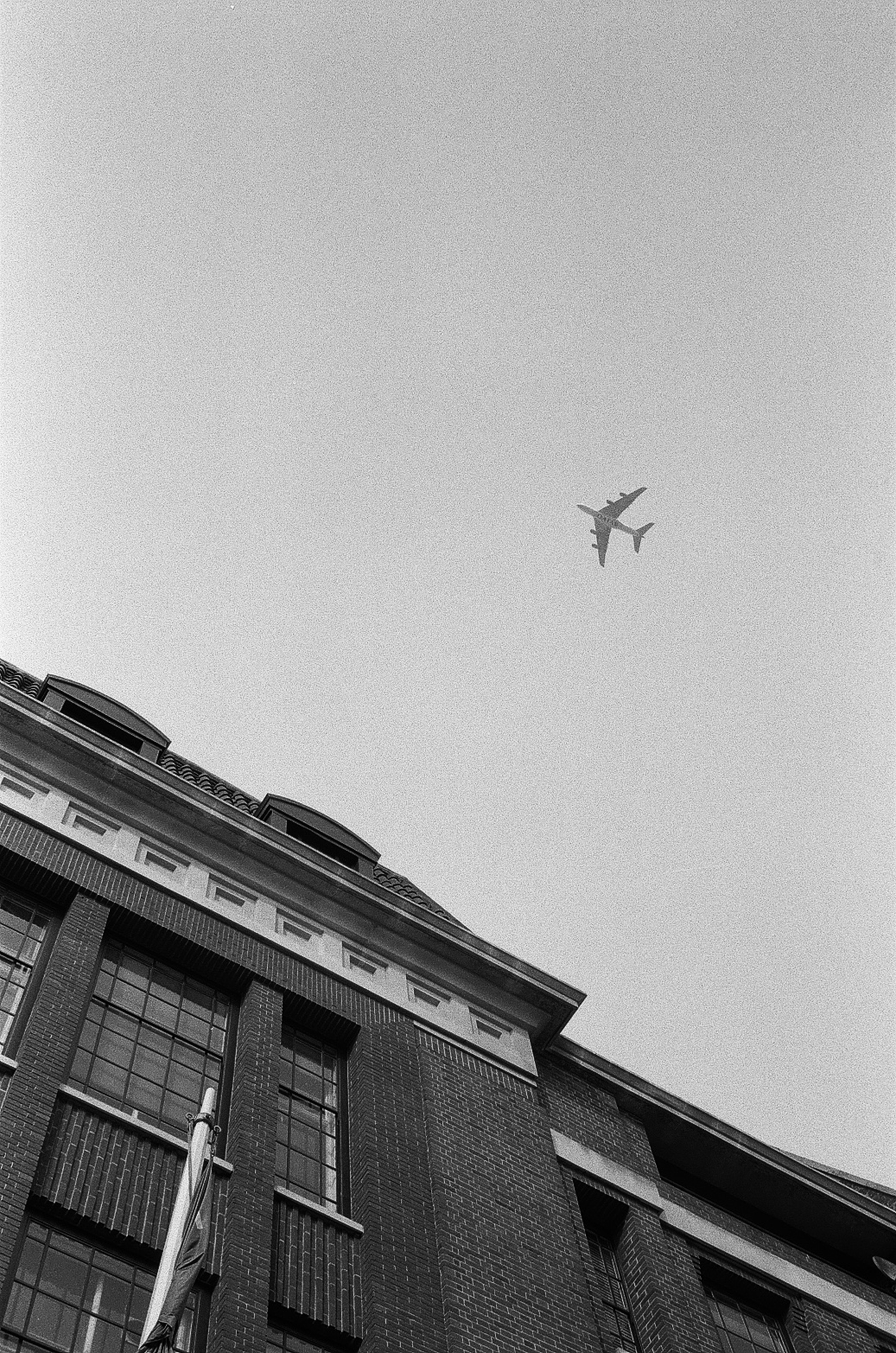 a black and white photo of an airplane flying over a building