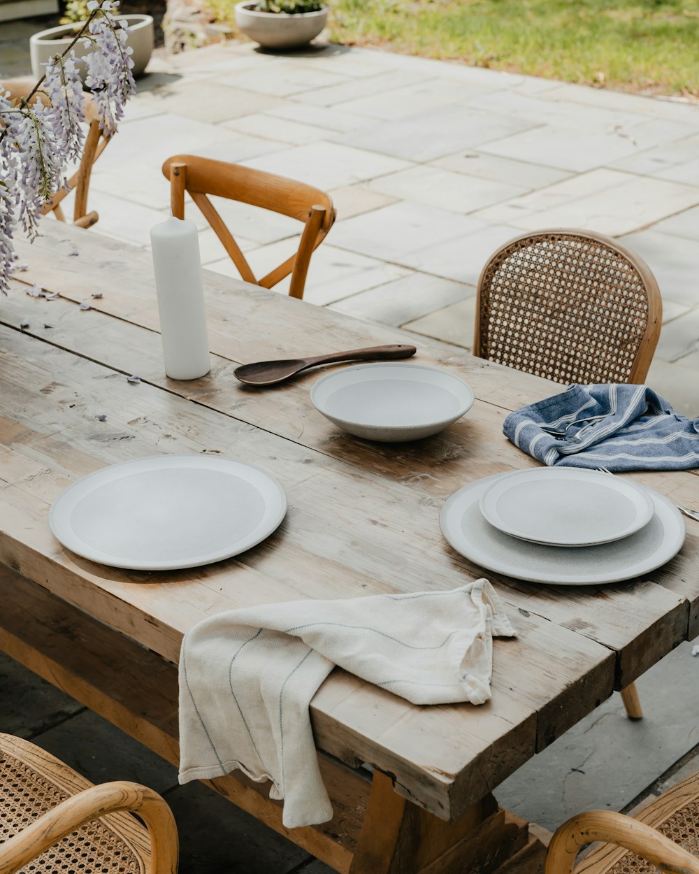 a wooden table topped with white plates and a vase filled with flowers