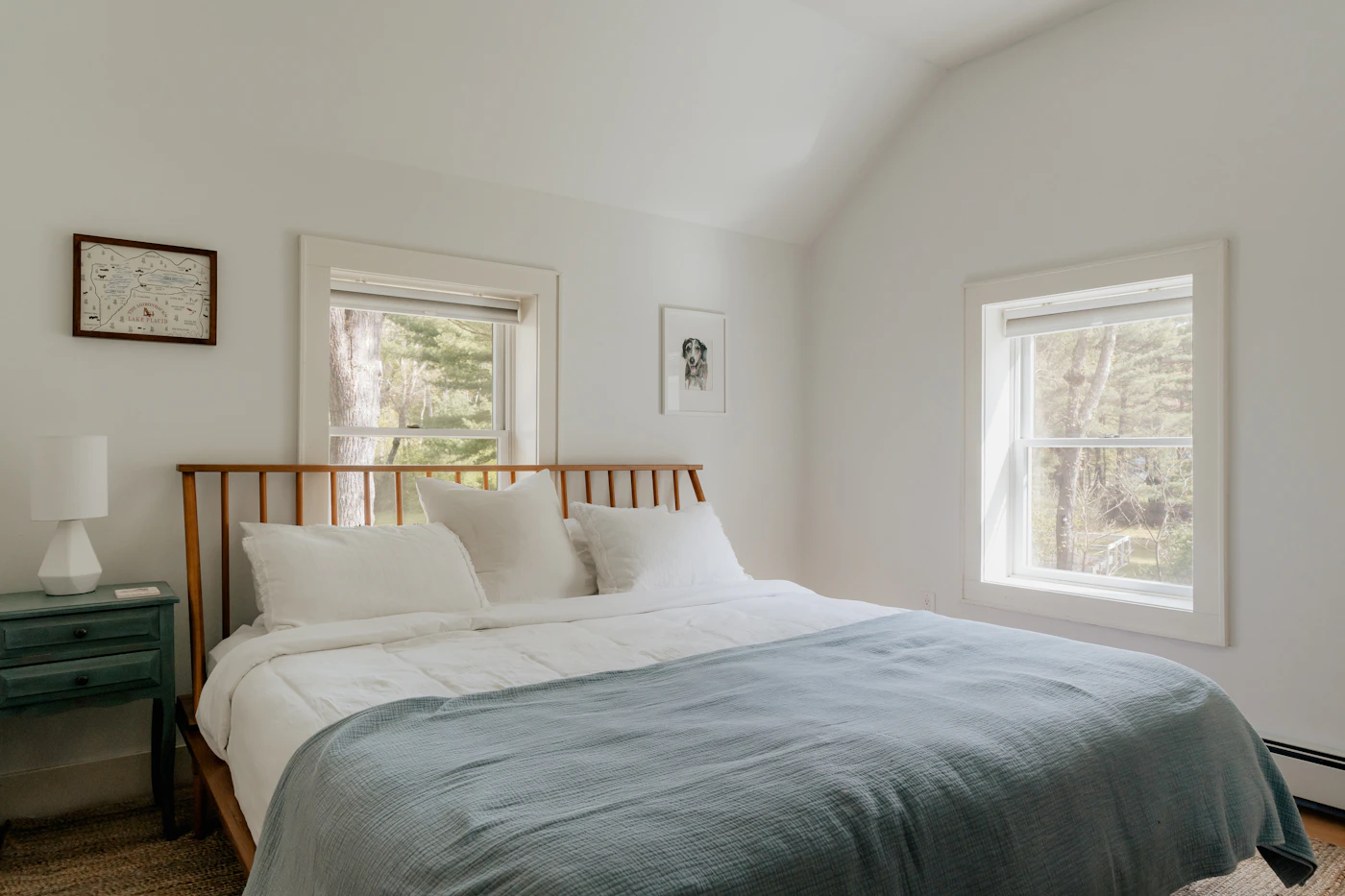 A whitewashed bedroom with a spindle bed and soft grey-blue linen in morning light