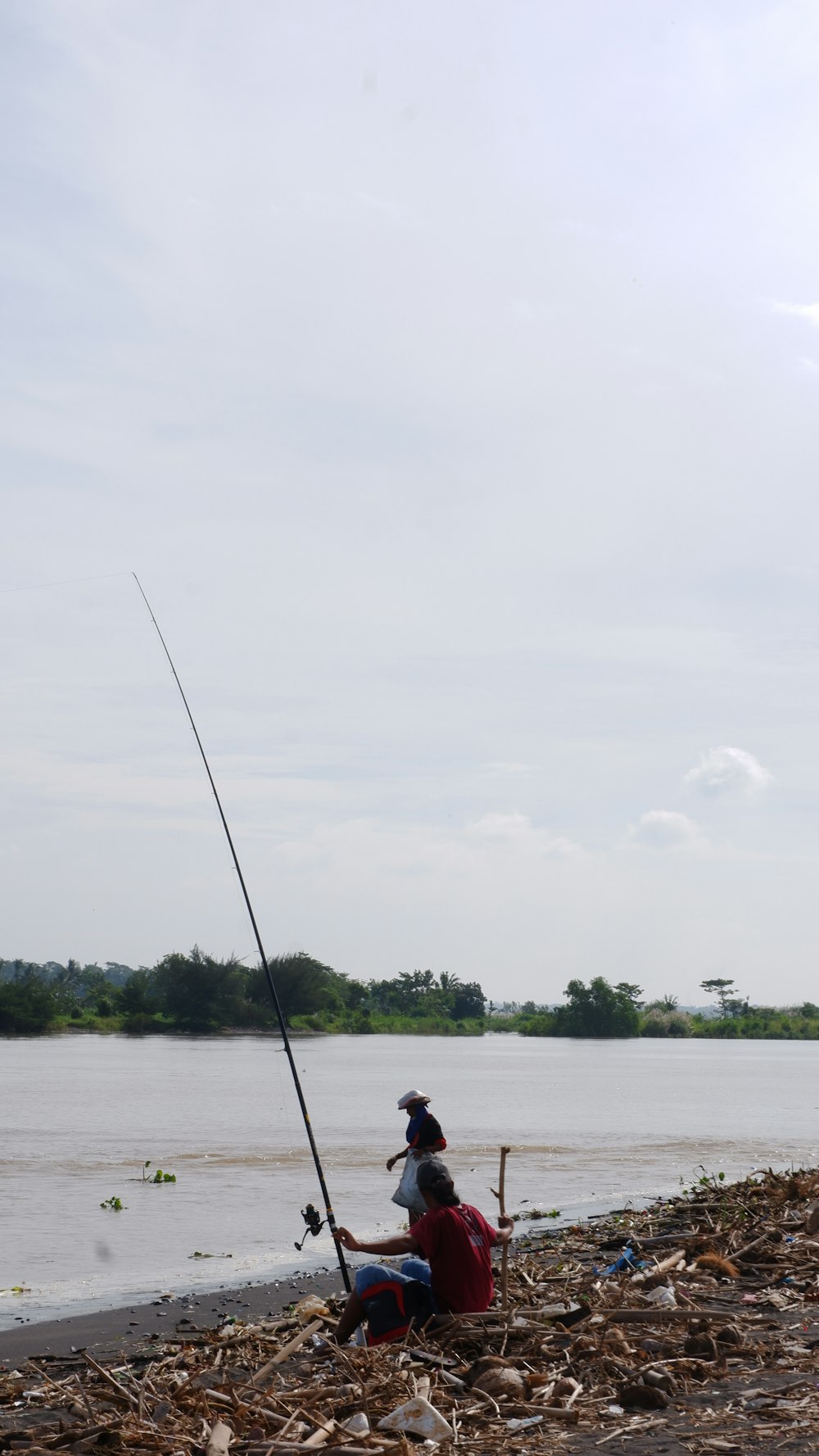 a man sitting on a beach next to a body of water holding a fishing pole