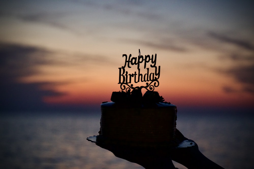 a person holding a birthday cake with a sunset in the background