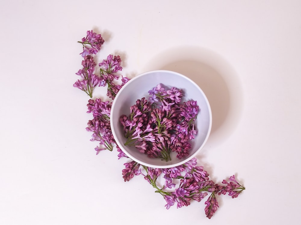 a white bowl filled with purple flowers on top of a table