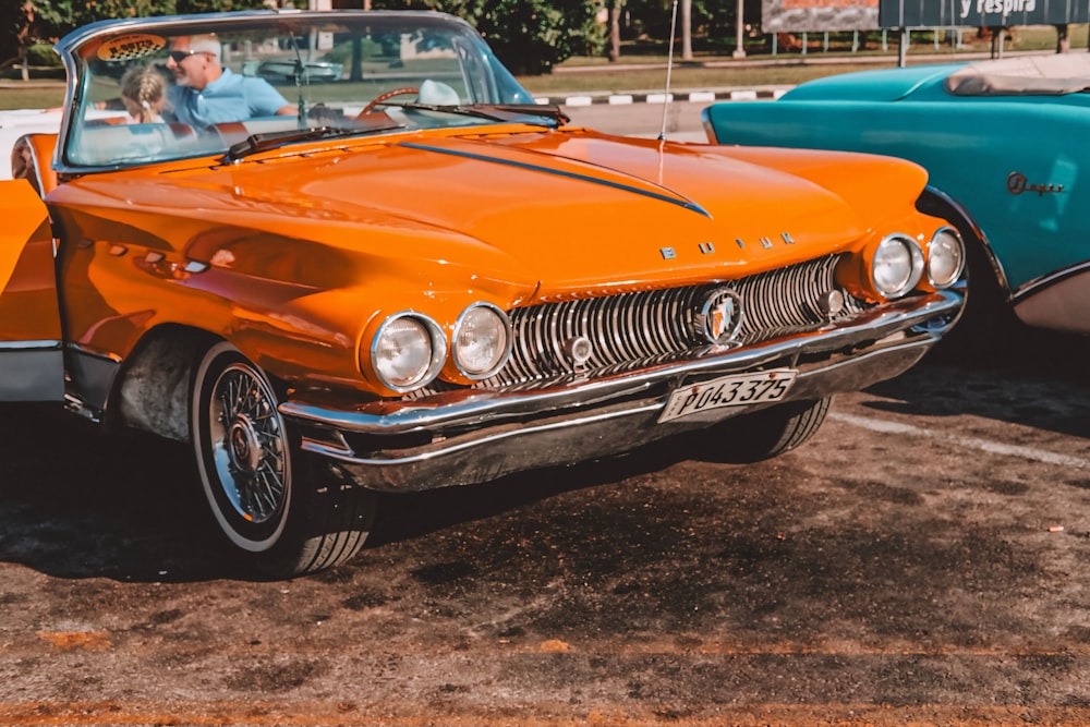 an orange convertible car parked next to a blue convertible car