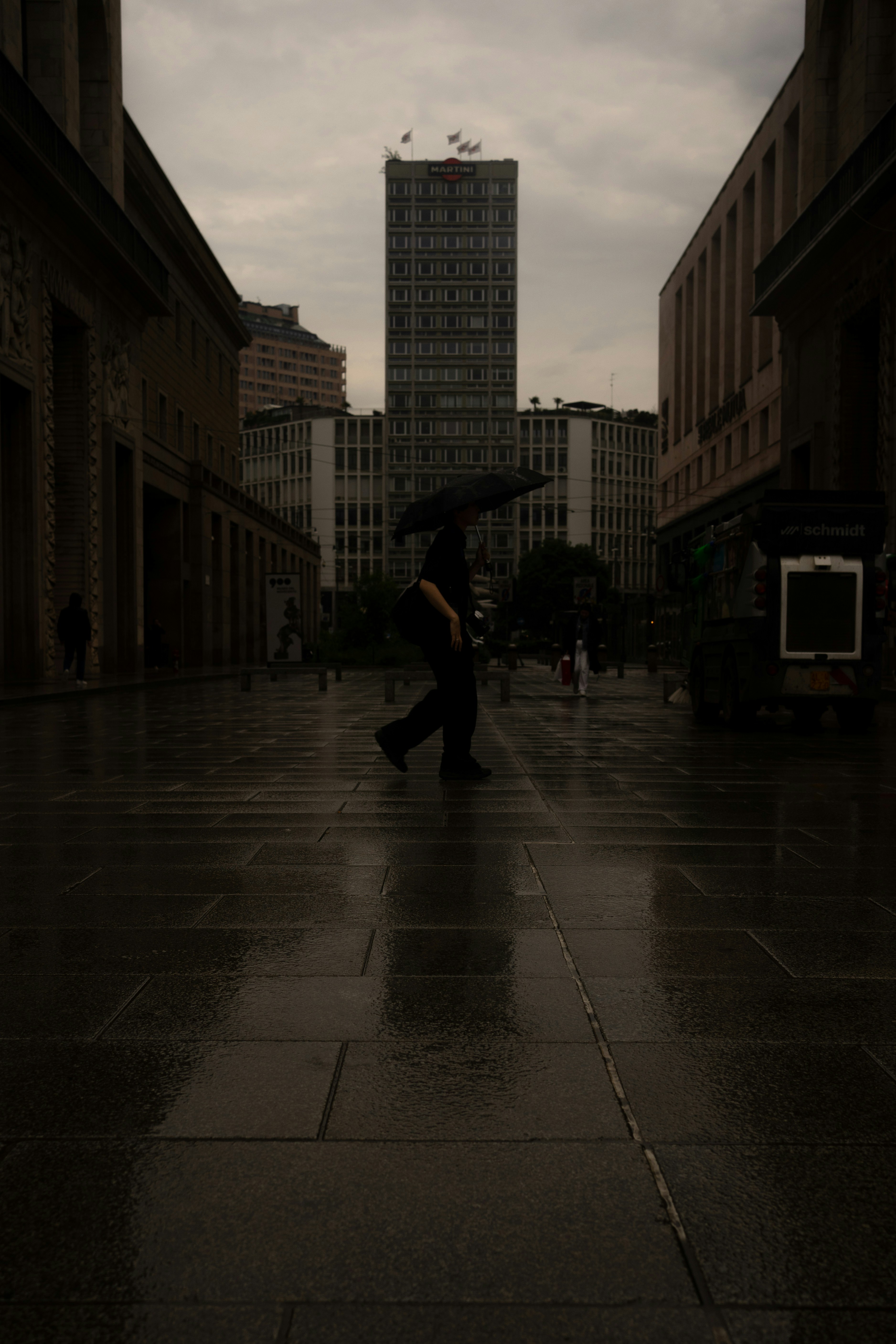 eine Person, die mit einem Regenschirm in der Hand eine Straße entlanggeht