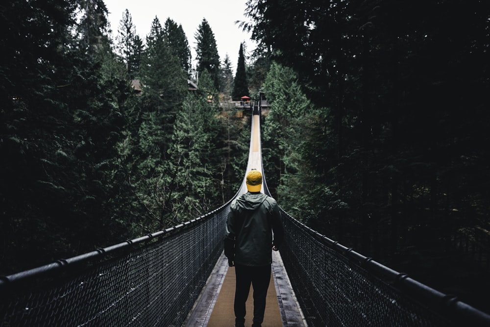 a man walking across a suspension bridge with trees in the background