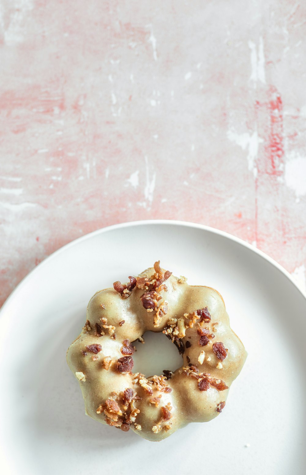 a white plate topped with a donut covered in nuts