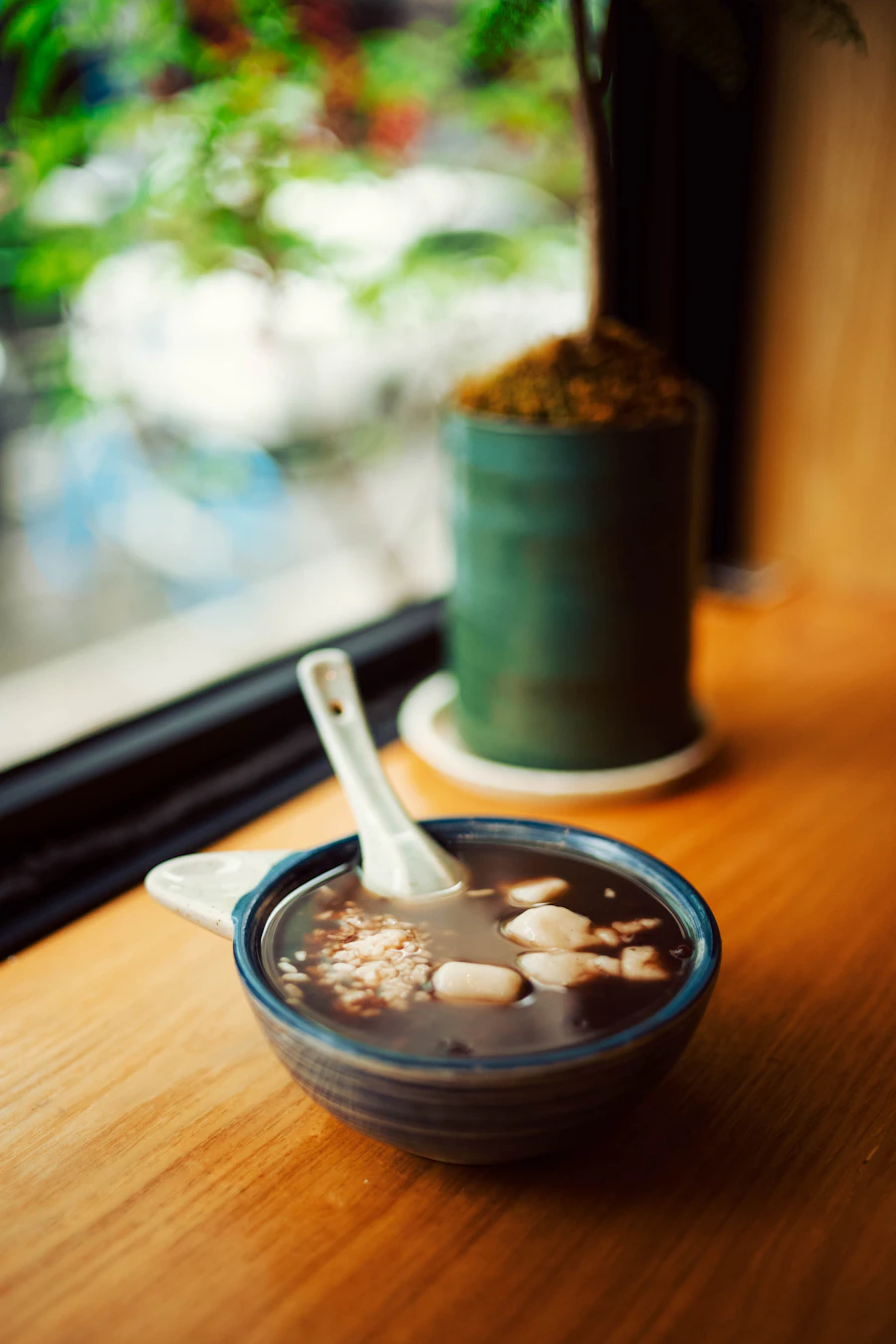 A dark bowl of chocolate rice porridge by a window