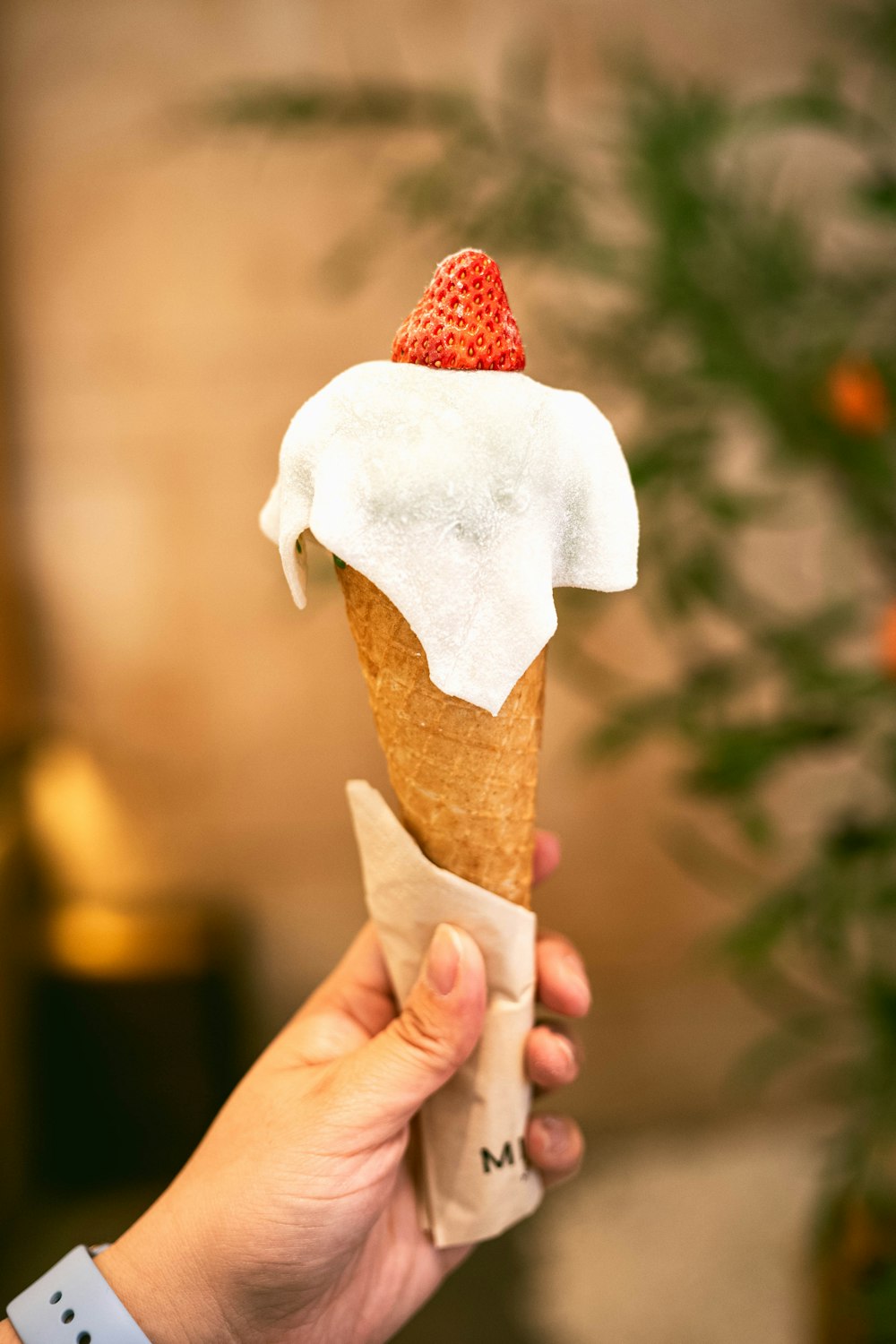a person holding a cone of ice cream with a strawberry on top