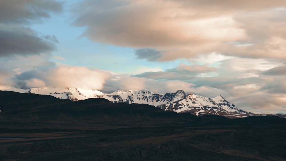 a mountain range covered in snow under a cloudy sky