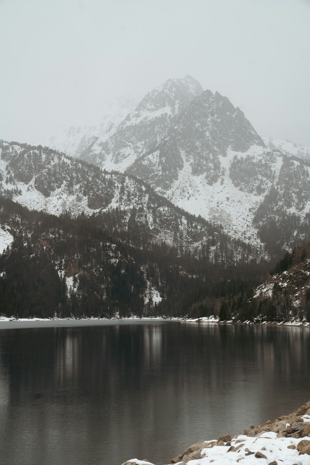 a mountain range covered in snow next to a lake