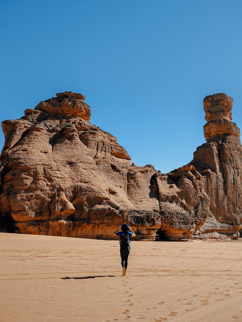 a person walking across a sandy beach next to large rocks