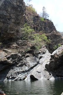 a man sitting on a rock next to a body of water