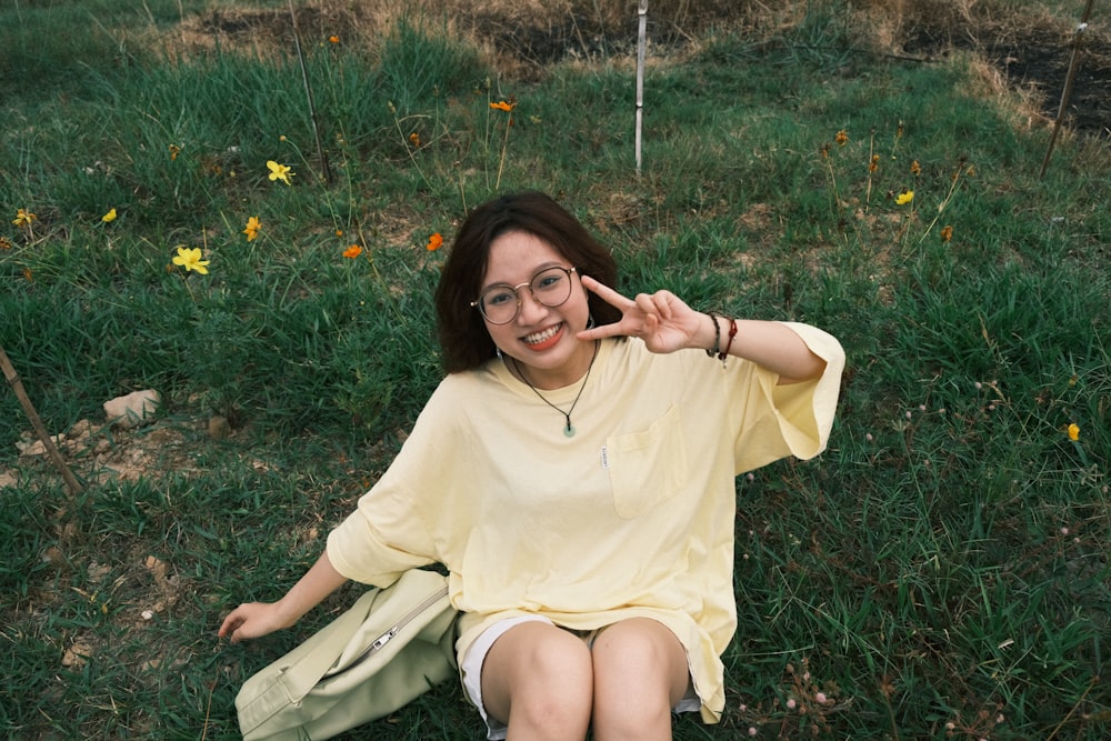 a woman sitting in the grass making a peace sign