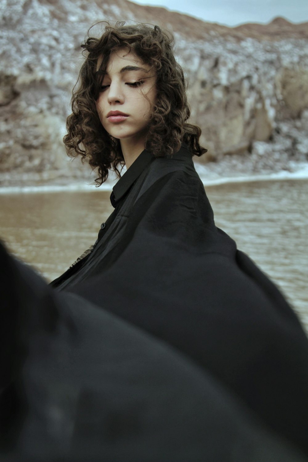 a woman with curly hair standing in front of a body of water