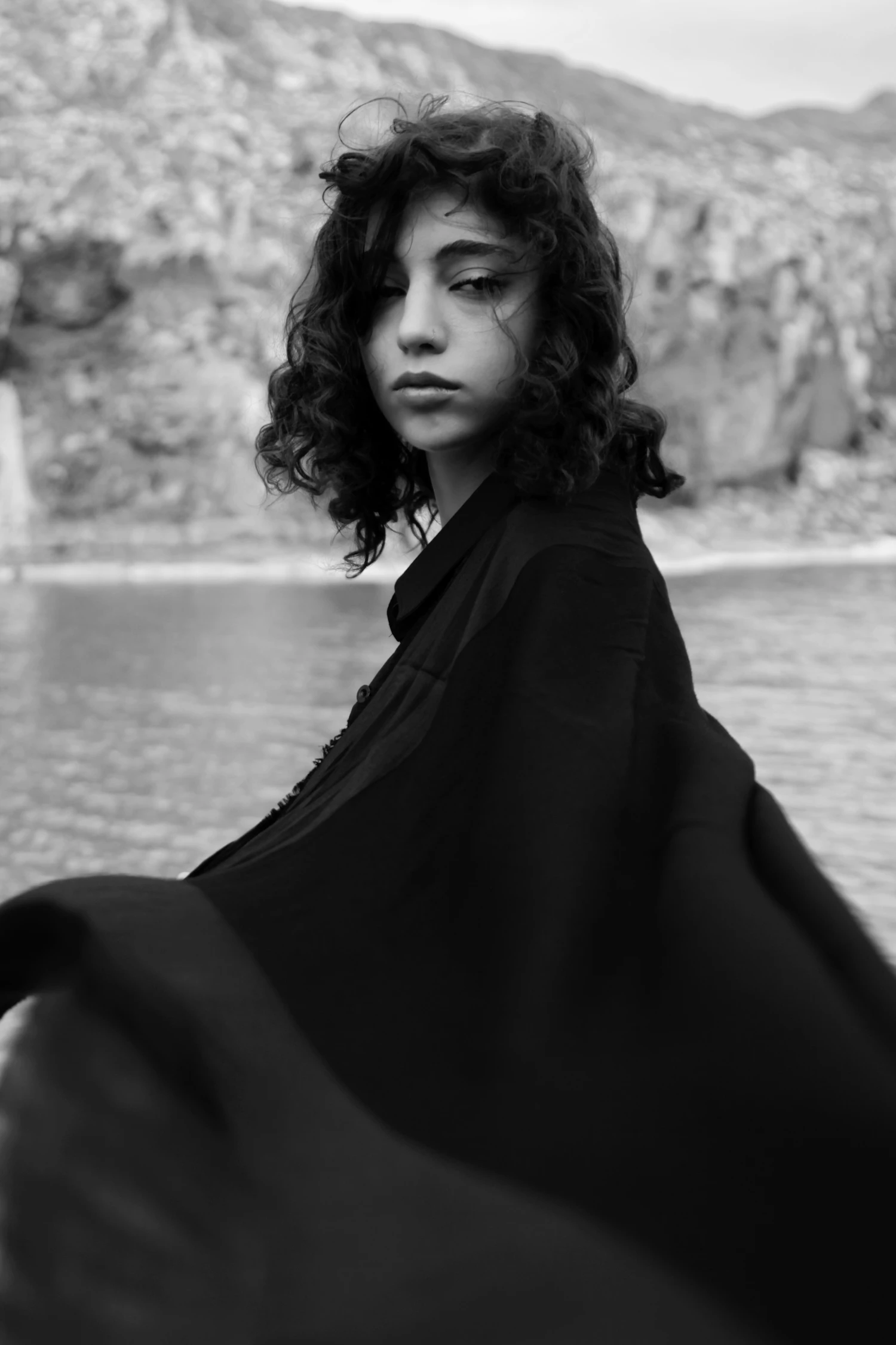 A figure gathering a length of black cloth, water behind