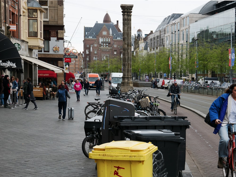 a woman riding a bike down a street next to a yellow trash can