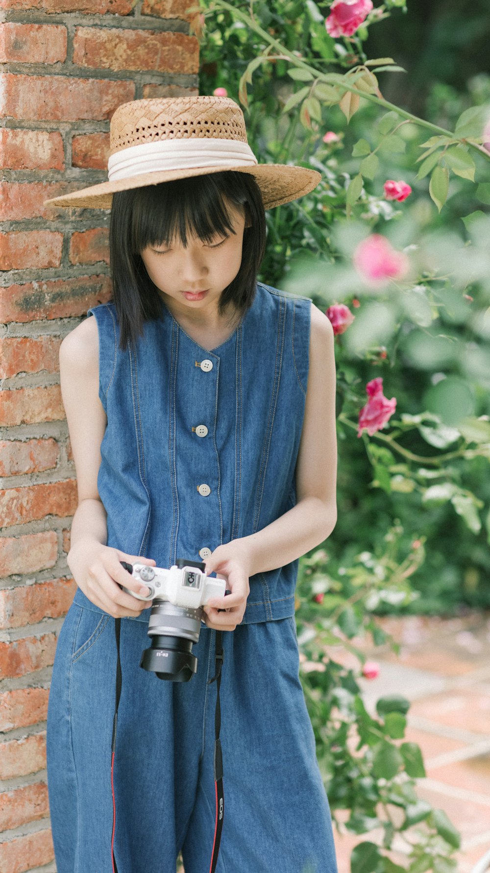 a girl in overalls and a hat holding a camera