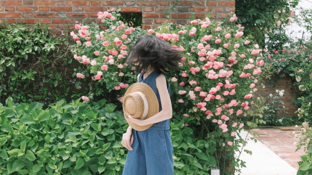 a woman standing in front of a bush with pink flowers