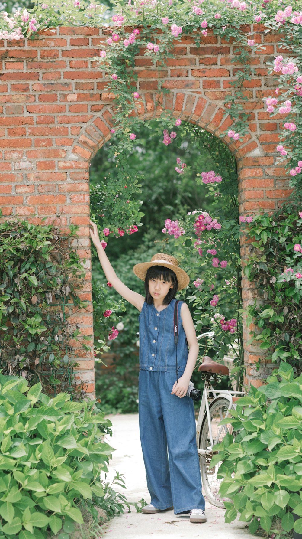 a woman in overalls and a hat standing in a garden