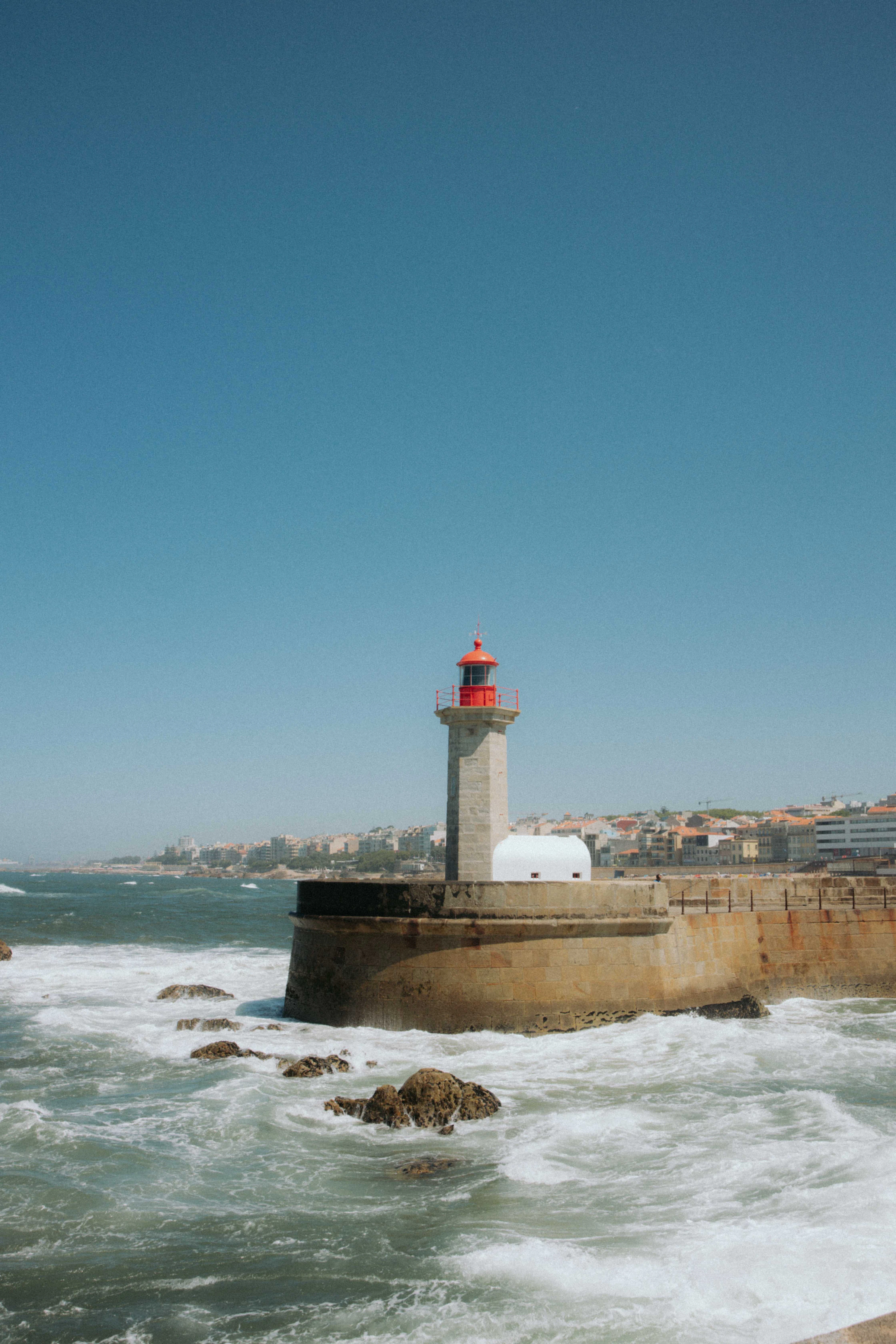 Waves crash around the red-and-white Felgueiras Lighthouse at the mouth of the Douro River in Porto.