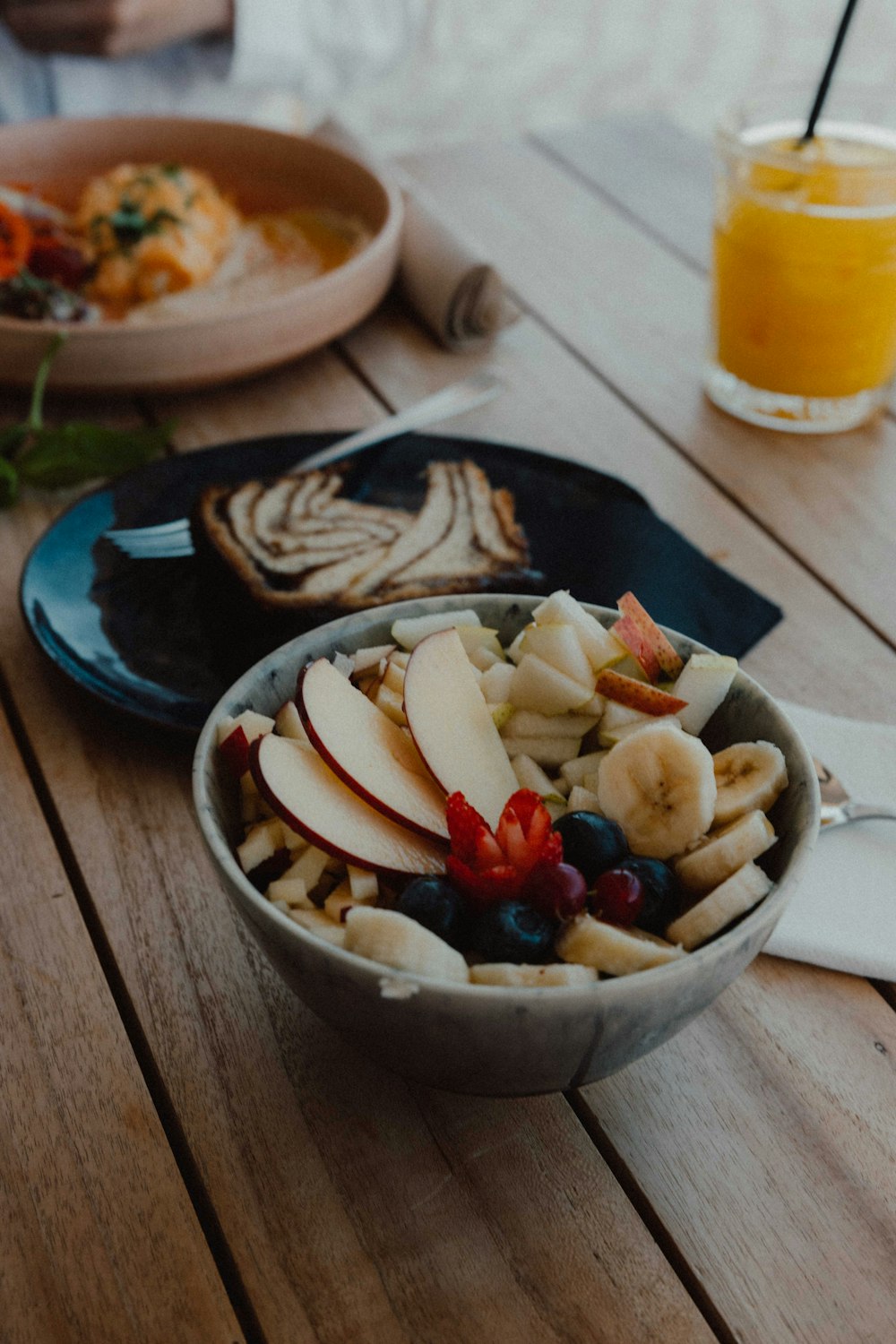 a bowl of fruit sits on a wooden table