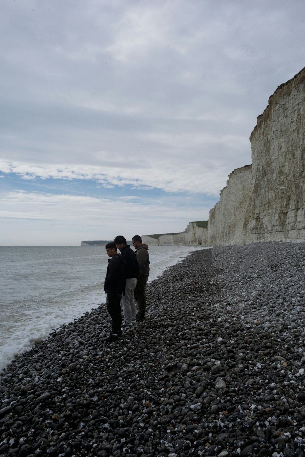 two people standing on a rocky beach next to the ocean