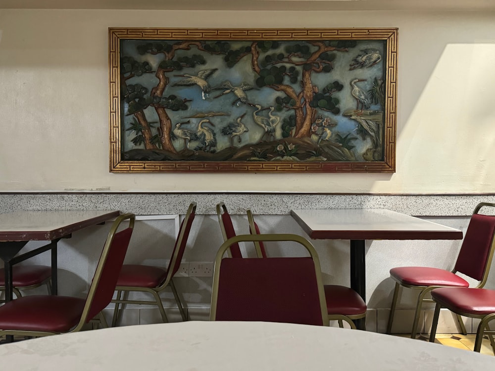 a painting hanging above a table with red chairs
