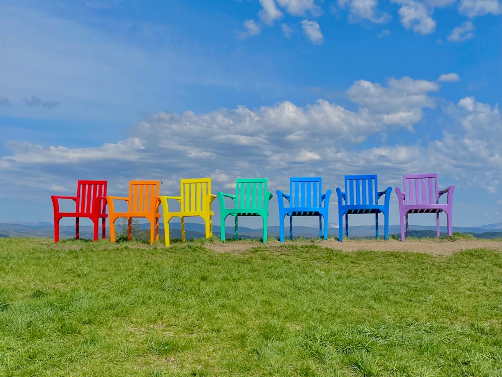 a row of colorful chairs sitting on top of a lush green field