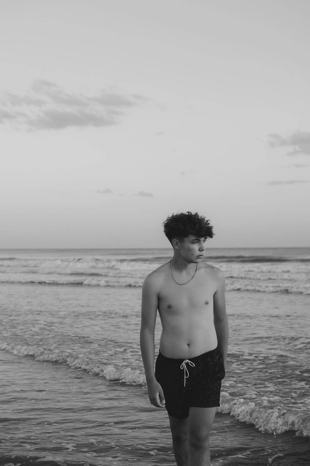 a shirtless man standing on a beach next to the ocean