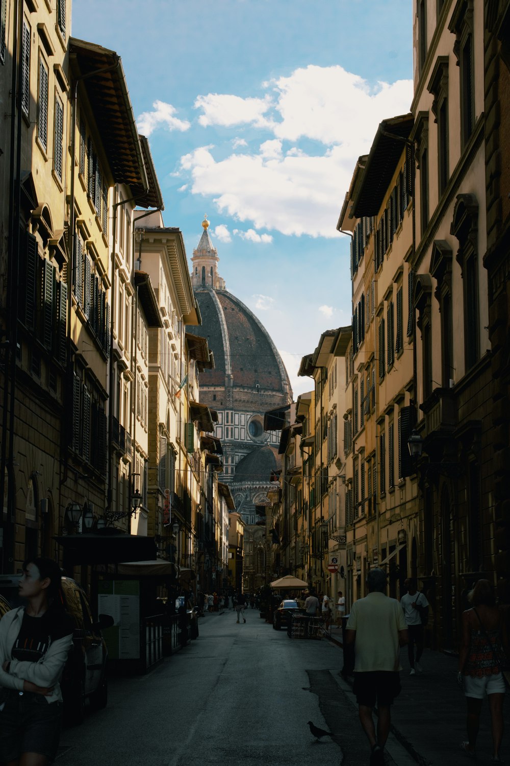 a narrow city street with buildings and a dome in the background