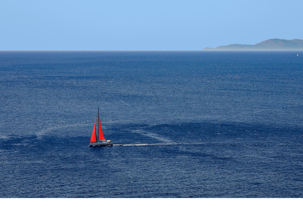 a red sailboat in the middle of the ocean